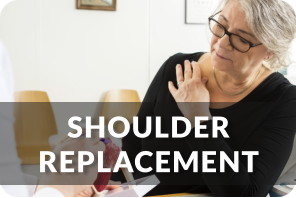 A doctor uses the model of a shoulder to show a patient the issue with her shoulder. The patient is holding her right shoulder with her left hand. Title reads; Shoulder Replacement