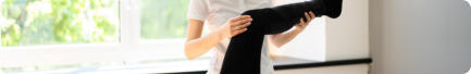 A patient is lying on a physical therapy table as a therapist lifts the patient's leg to work their knee.