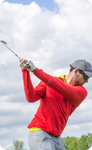 Photo of a senior man golfing on a sunny day. He is facing away from the viewer with the golf club raised over his shoulder as he completes his swing.