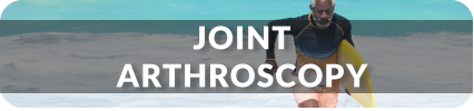 A senior man jogs out of the ocean onto the beach with a surfboard under his arm. Title reads: Joint Arthroscopy